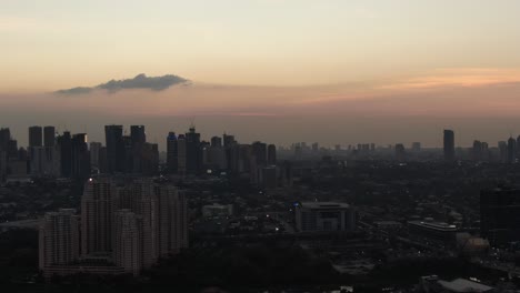 An-eerie,-hazy-tracking-drone-shot-of-twilight-showing-the-Ortigas,-Manila-skyline-as-traffic-leaves-the-city