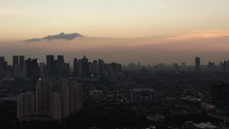 Un-Espeluznante-Y-Borroso-Disparo-De-Dron-De-Seguimiento-Del-Crepúsculo-Que-Muestra-El-Horizonte-De-Ortigas,-Manila-Mientras-El-Tráfico-Sale-De-La-Ciudad