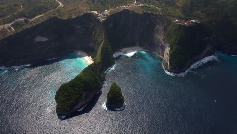 drone flying forward tilt down above kelingking beach on nusa penida island over the seashore green peninsula yellow sand