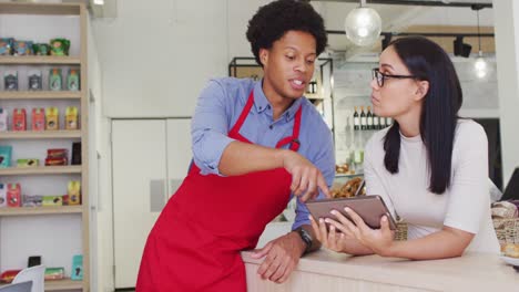 Video-of-happy-diverse-female-owner-and-male-waiter-working-with-tabletat-cafe-shop