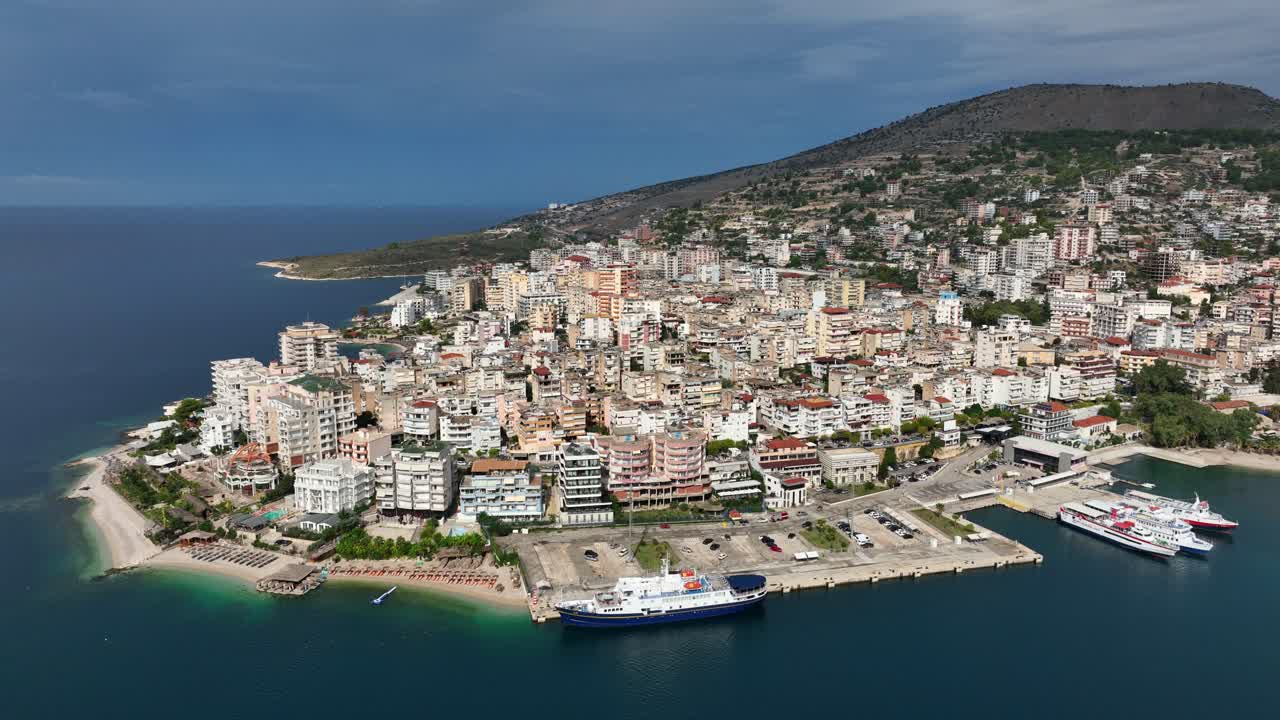 Wide view of Saranda's curved bay and surrounding cityscape with bright afternoon light, panoramic establishing