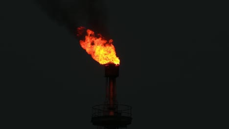 a wide shot of a large flaming torch above a gas tower illuminating the night sky