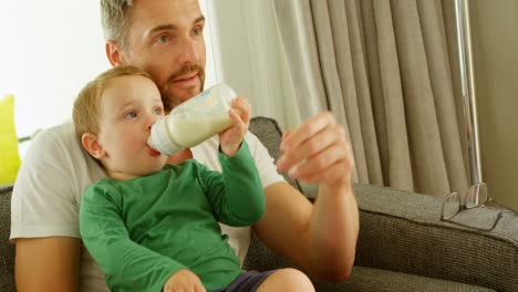 niño en el regazo del padre bebiendo leche en el sofá 4k