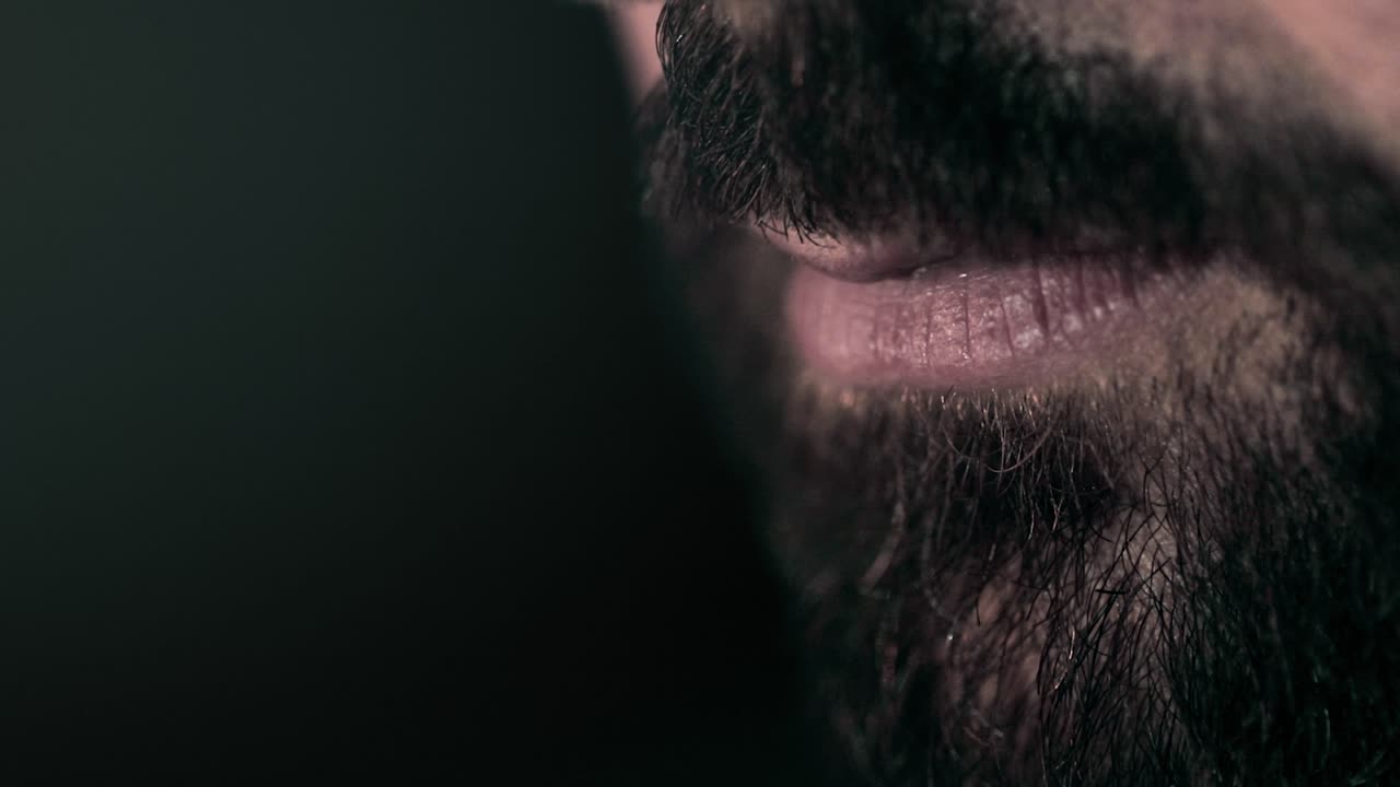 Super close up isolation on man's black beard and lips. Dark ambient background
