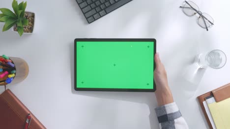 vista de arriba hacia abajo de una computadora portátil con pantalla verde simulada pantalla chromakey en un escritorio de oficina de madera al lado de la libreta con bolígrafos, gafas y un vaso de agua.
