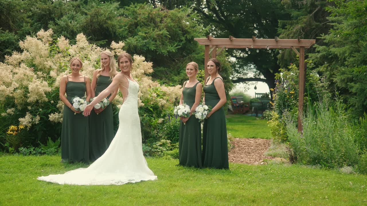 Bride tosses the train of dress while posing with smiling bridesmaids in garden