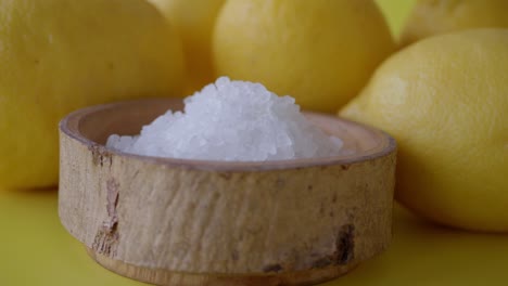 close up of salt in wooden bowl with lemons in background