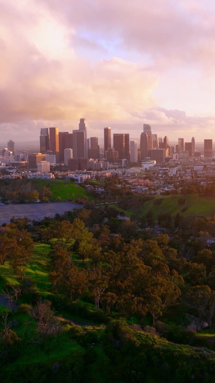 Vista do horizonte do centro de Los Angeles com arranha-céus e palmeiras. O congestionamento de tráfego é visível em áreas urbanas durante a hora do rush. A infraestrutura da cidade e o desenvolvimento urbano são mostrados.