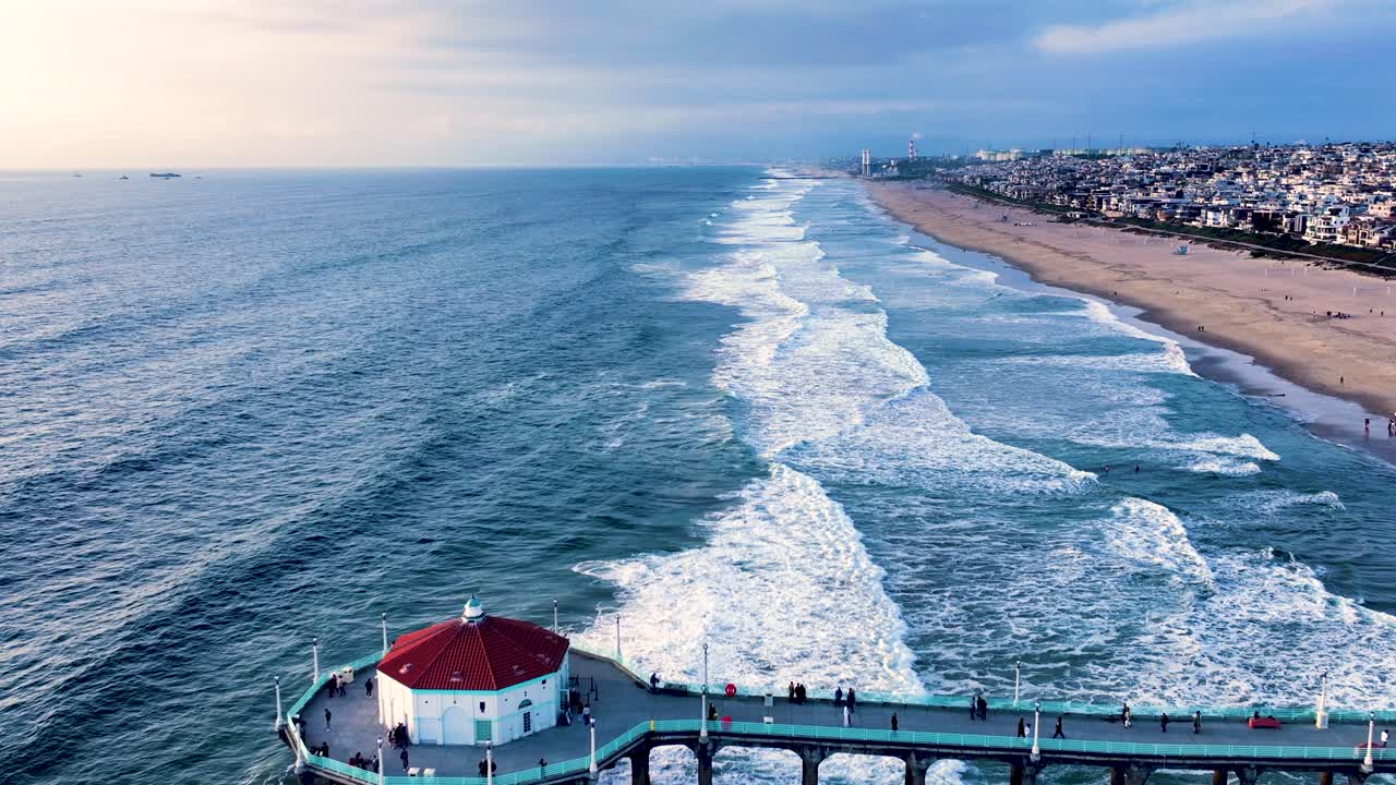 Drone estabilshing dolly of iconic Manhattan Beach Pier stretching into ocean with turquoise water, Los Angeles, California