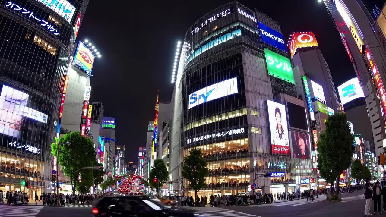 Fisheye view of a bustling city intersection at night, with bright neon signs and video billboards
