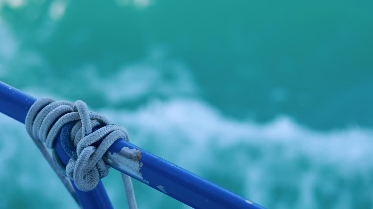 Close-up of a rope knot on a blue railing against the turquoise ocean, capturing movement and texture in natural light
