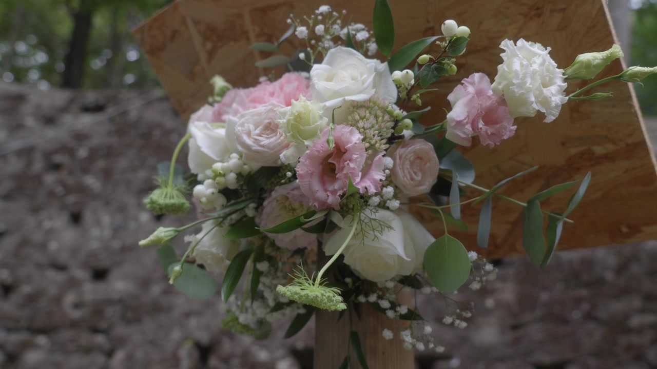 Nærbillede af pastelrosa og hvid blomsterbuketdekoration ved udendørs bryllupsceremoni.