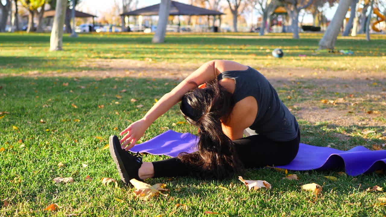 una mujer estirándose durante un entrenamiento a cámara lenta en una alfombra de yoga morada en un parque al atardecer