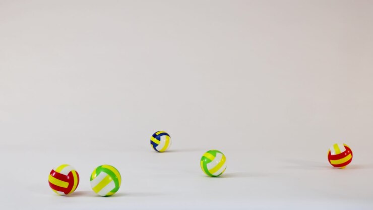 Small colorful volleyballs fall, bounce, and roll across a clean white studio floor surface