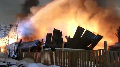 a dramatic night scene as firefighters spray water from an aerial hose onto a blazing building engulfed in flames and thick smoke. emergency crews battle the fire under harsh conditions.