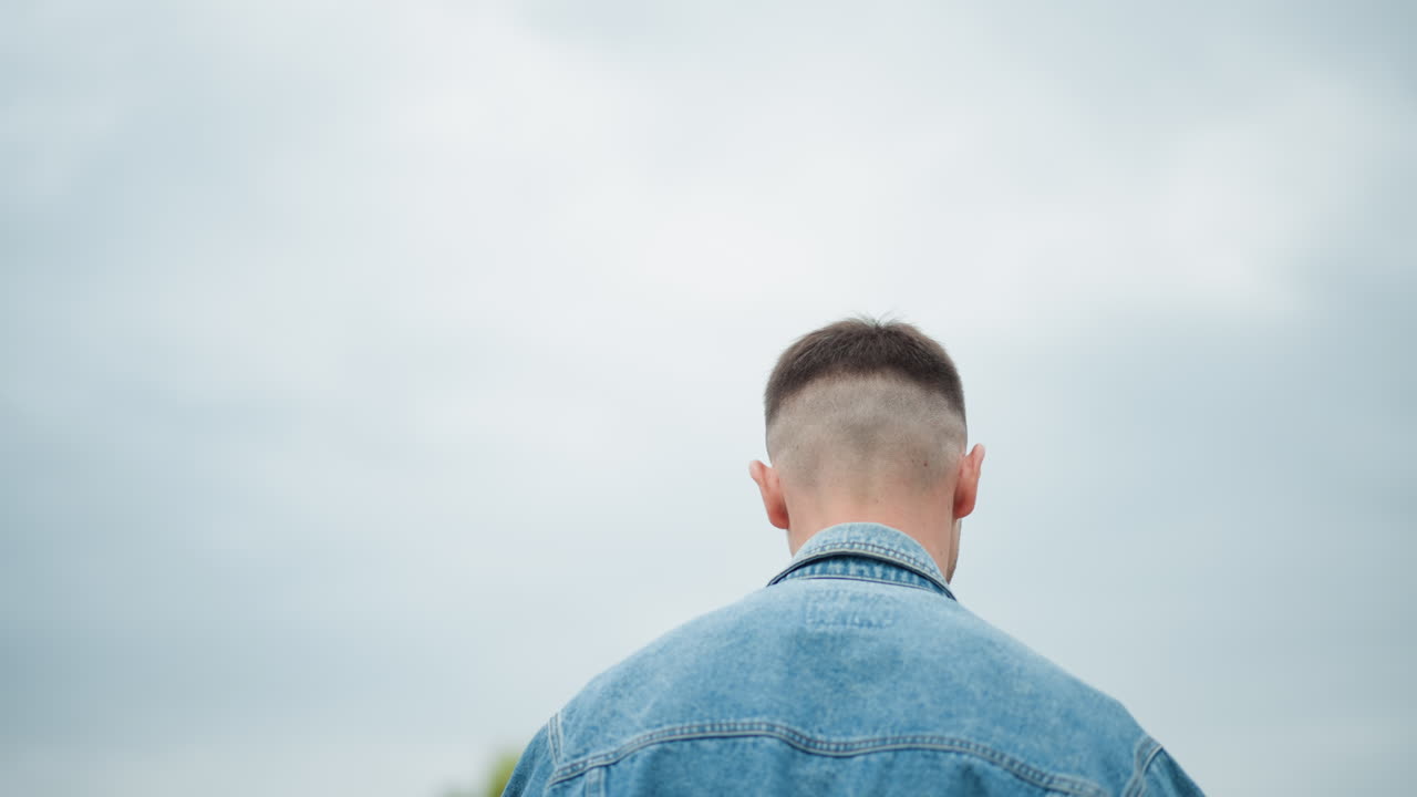 Individual in denim notices car beneath clouds, Casual traveler confronts parked vehicle under overcast skies, Tourist dressed in denim observes stationary automobile in parking lot on cloudy day