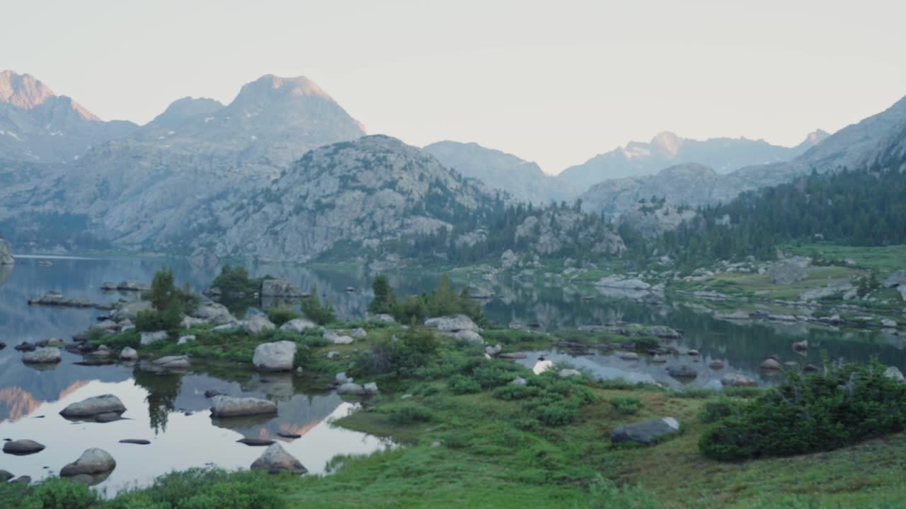 paisaje alpino sereno con lago tranquilo y montañas al amanecer, panorámica de gran ángulo