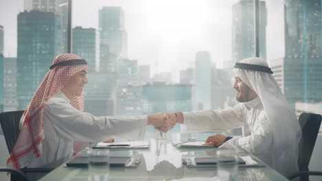 dos empresarios emiratíes alegres en kandura tradicional blanca sentados en la oficina y firmando el contrato. los socios comerciales se estrechan la mano en una inversión lucrativa. el concepto de empresario saudí, emiratí y árabe.