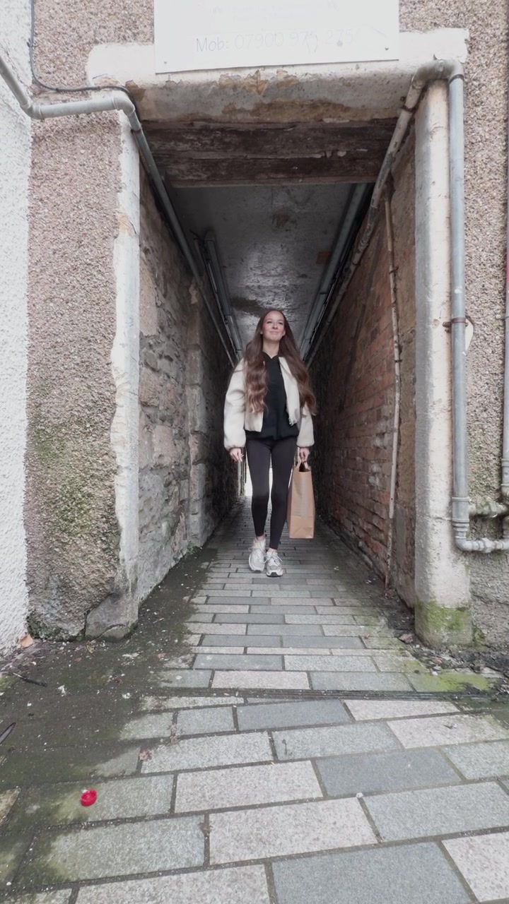 Vertical view, teenage girl walking through a narrow alley carrying a shopping bag, illustrating everyday urban life, independence and the journey home