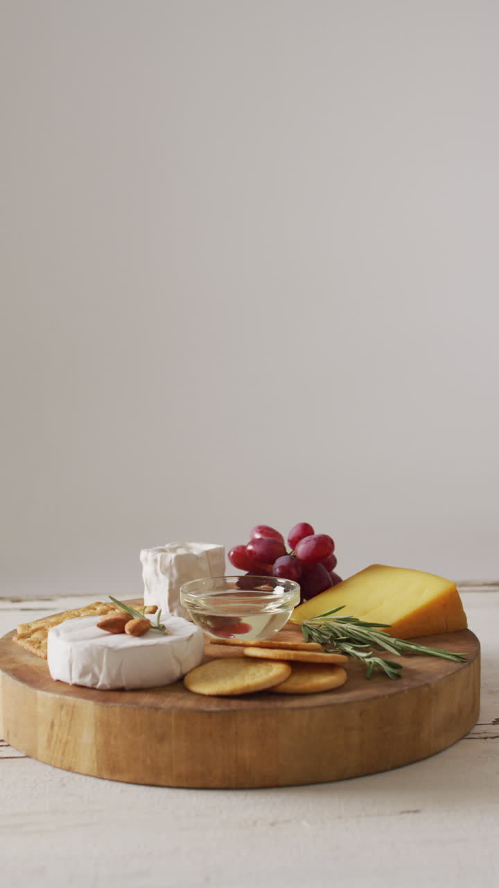 video vertical de algunos tipos de queso, galletas y uvas rojas en una tabla de cortar de madera