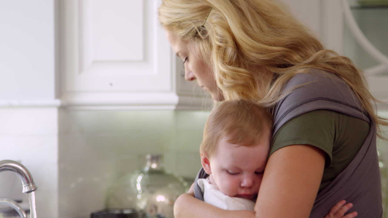 Mère occupée avec un bébé en porte-bébé à la maison, filmé en R3D