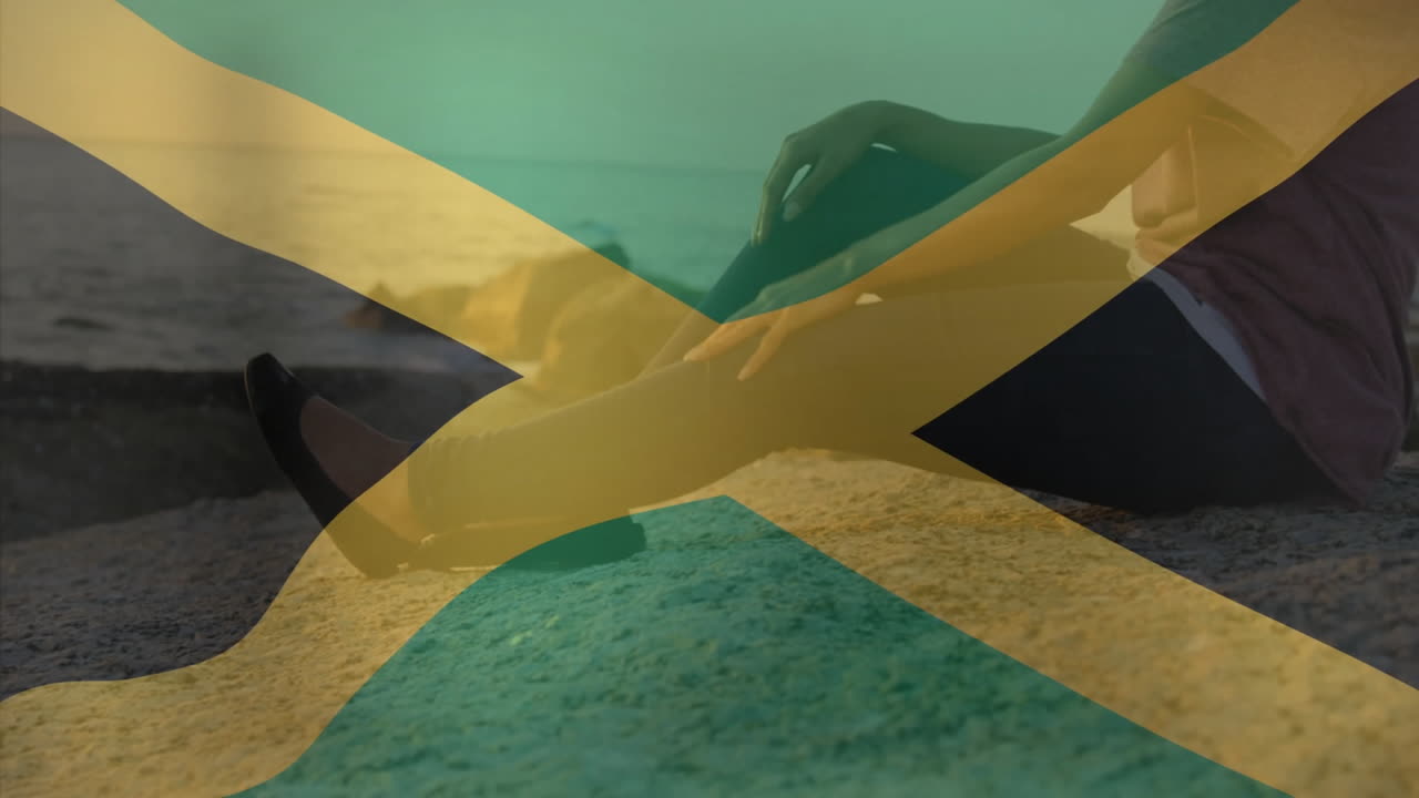 Sitting on rocky beach, person with Jamaican flag overlay at sunset animation