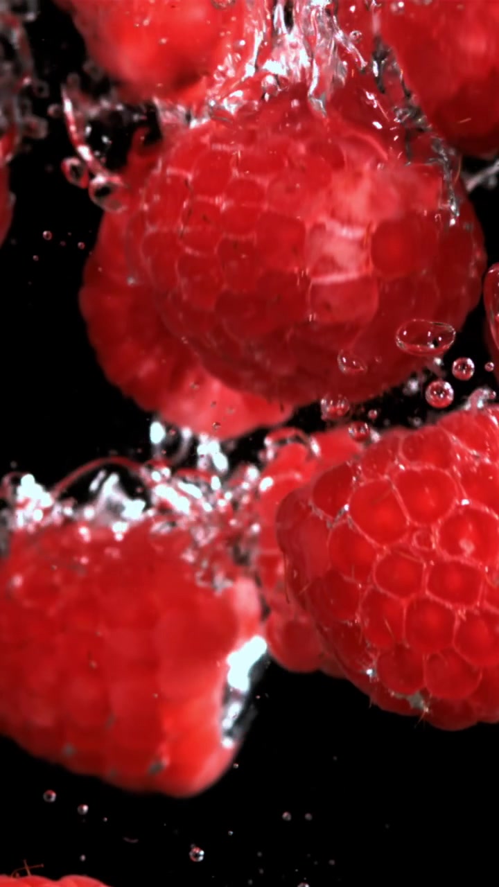 Vibrant Red Raspberries Falling into Clear Water with Bubbles