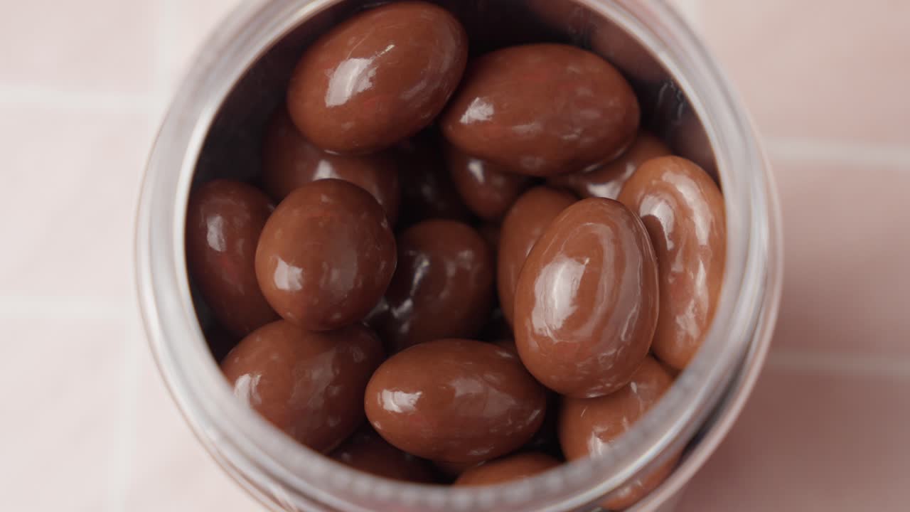 Pick up milk chocolate covered almonds, hazelnuts and raisins from clear jar with your hand