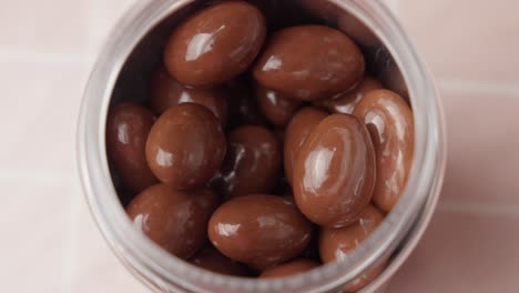 pick up milk chocolate covered almonds, hazelnuts and raisins from clear jar with your hand