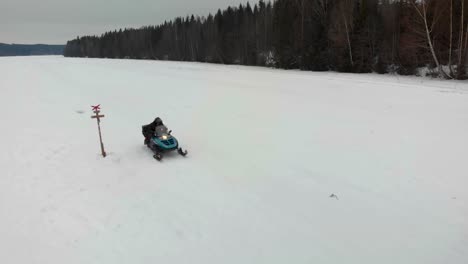 aerial shot of a man starting his snowmobile and driving away on indalsalven in timra, sundsvall, sweden.