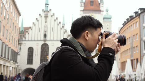 young asian traveling backpacker in city centre in europe. man taking photos in marienplatz square, munich, germany