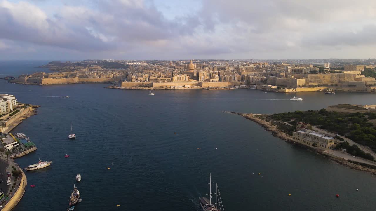 Stunning aerial vista capturing Valletta's fortified peninsula jutting into the Mediterranean, with sailboats and yachts dotting the calm blue waters of Grand Harbour under golden afternoon light