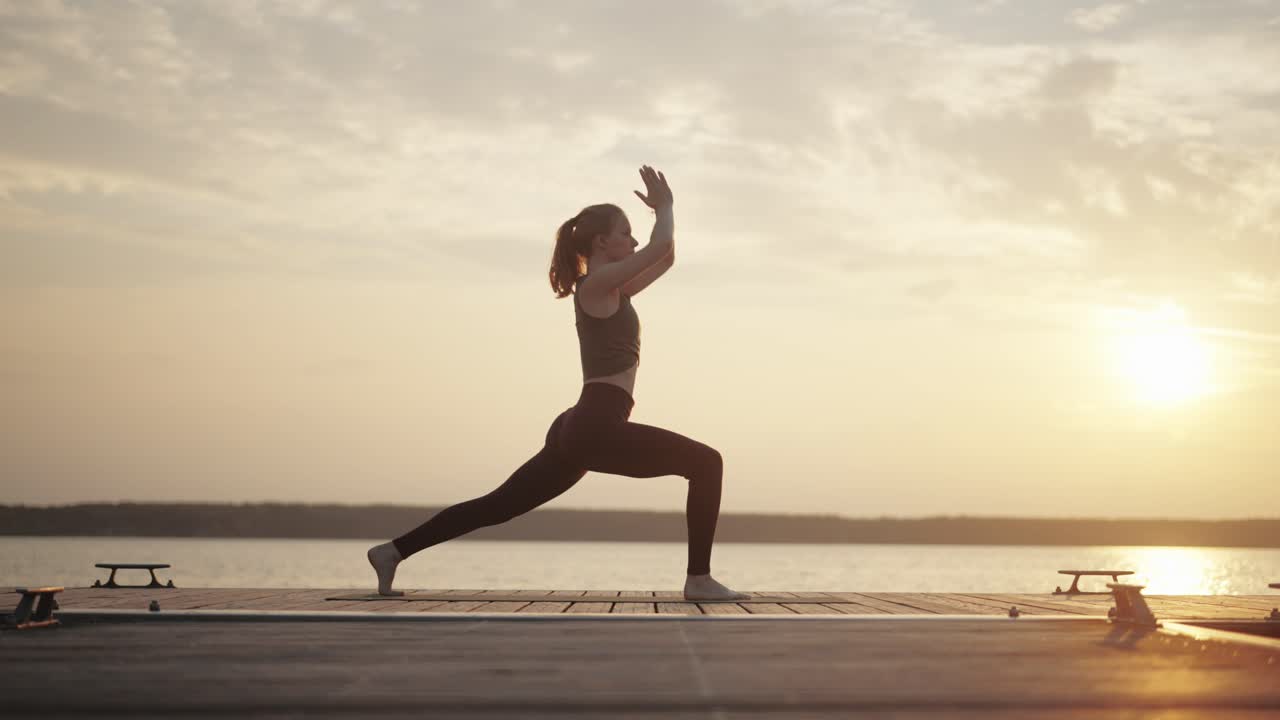 Female yogi practicing powerful yoga on jetty at sunset, slow motion