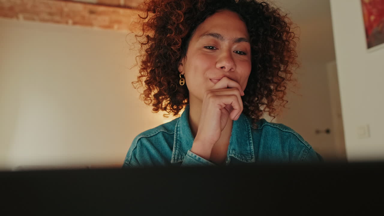 Young Woman with Curly Hair Looking at Screen and Smiling