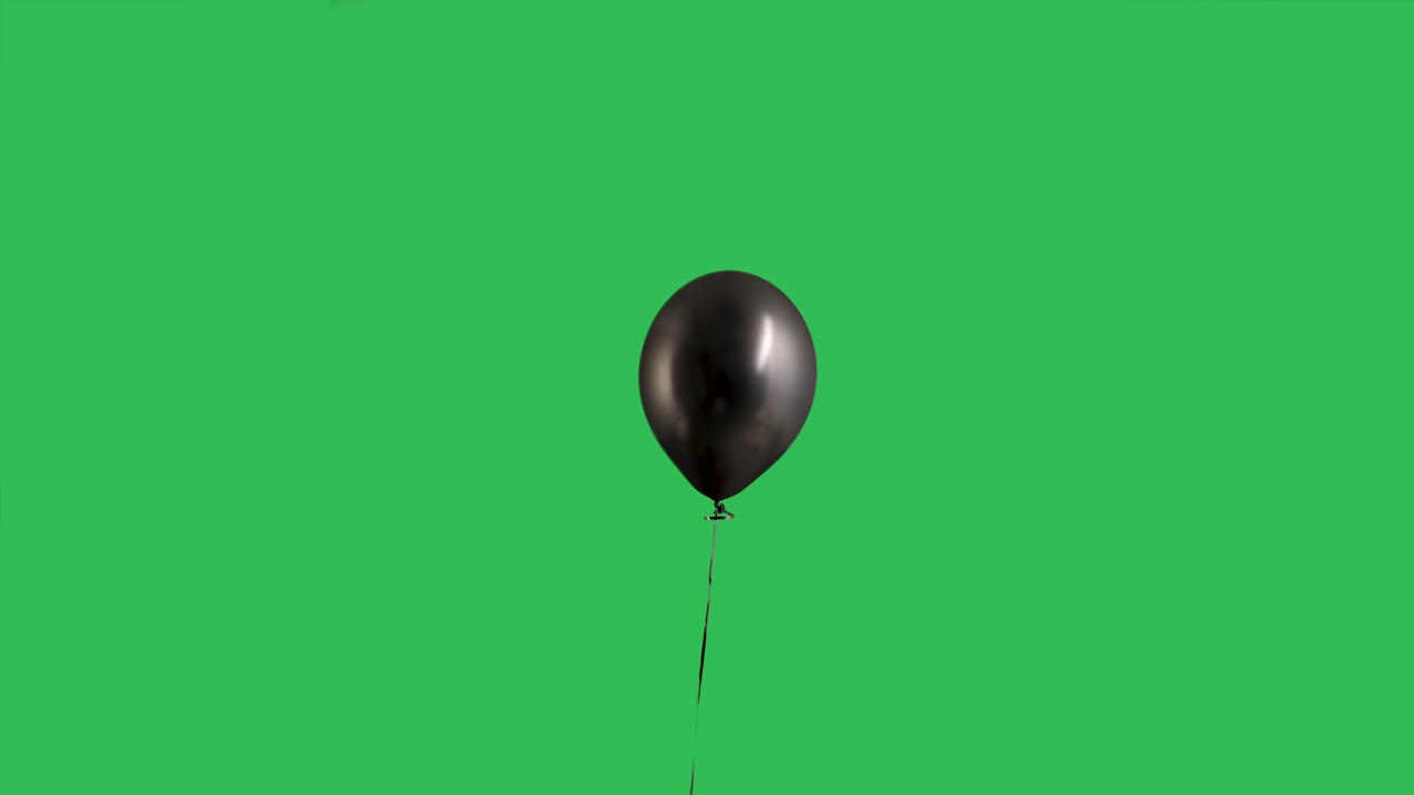 Palloncino nero sospeso in aria su sfondo green screen chroma key. Palloncino a elio isolato con nastro. Compleanno, decorazione per feste, festività, sorpresa, regalo. Slow motion.