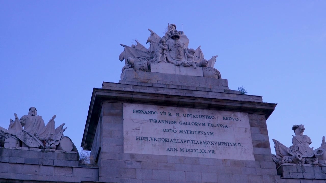 Un plan en contre-plongée des sculptures en pierre ornées et de l'inscription latine sur la porte de Tolède à Madrid au crépuscule. Convient aux documentaires de voyage et d'histoire