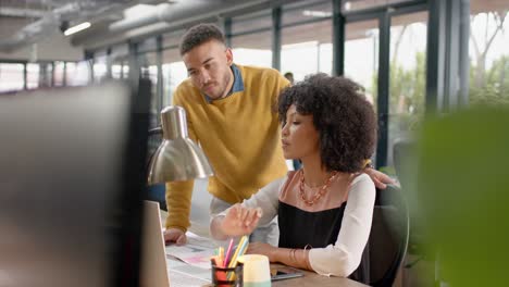 Diverse-man-and-woman-discussing-over-a-computer-at-office