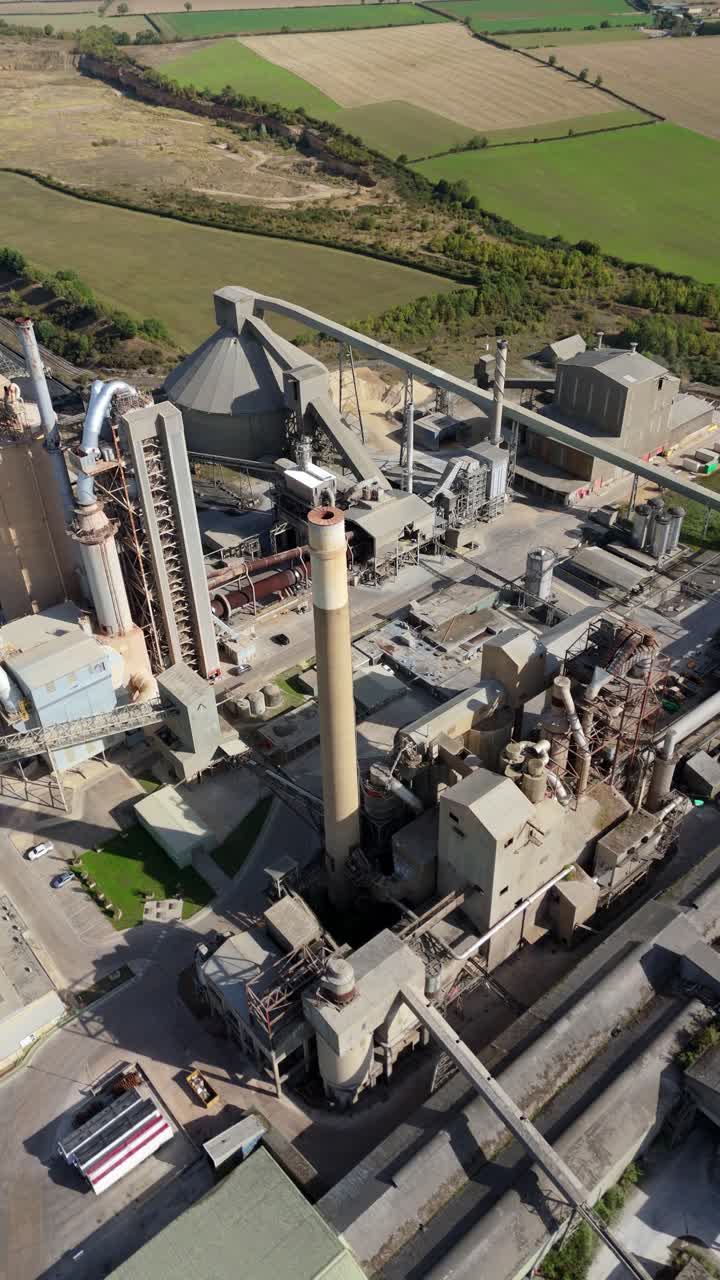 Aerial shot of cement factory infrastructure with pipework, silos, and chimneys in operation near Stamford, UK