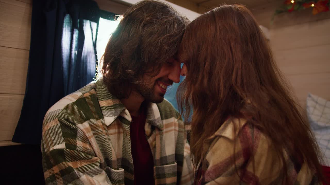 Close-up shot of a romantic scene, a brunette guy in a green checkered shirt rubs his forehead against his brunette girlfriend in a checkered shirt while relaxing in a trailer in a camp during a picnic in the summer