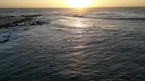 Bird's-eye-view-of-surfers-bobbing-on-the-waves-at-sunset-near-the-coastline