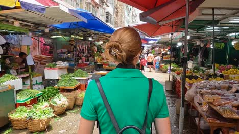 pov walking behind female tourist wearing green dress with backpack through markets at mong kok, hong kong