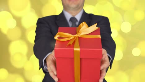 un hombre en un traje de negocios con una corbata está sosteniendo una caja de regalos roja. un hombre da un regalo. un hombre de negocios con un regalo en sus manos. fondo abstracto flash dorado parpadeando y brillo círculo luces bokeh.
