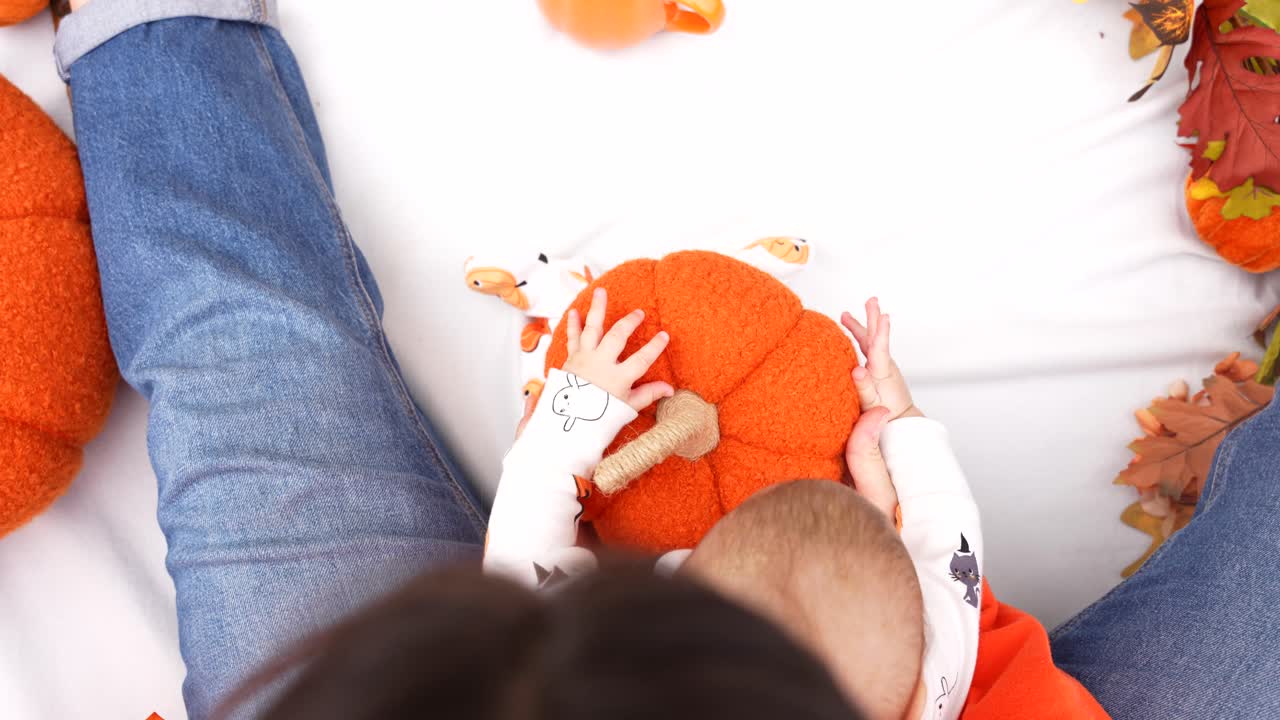Top down shot of an unrecognizable mom holding a fabric pumpkin to show textures to her baby in a Halloween setting, sensory game