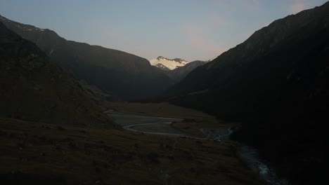 A-reverse-drone-shot-through-a-dark-valley-with-the-bright-peak-of-a-mountain-in-the-distance