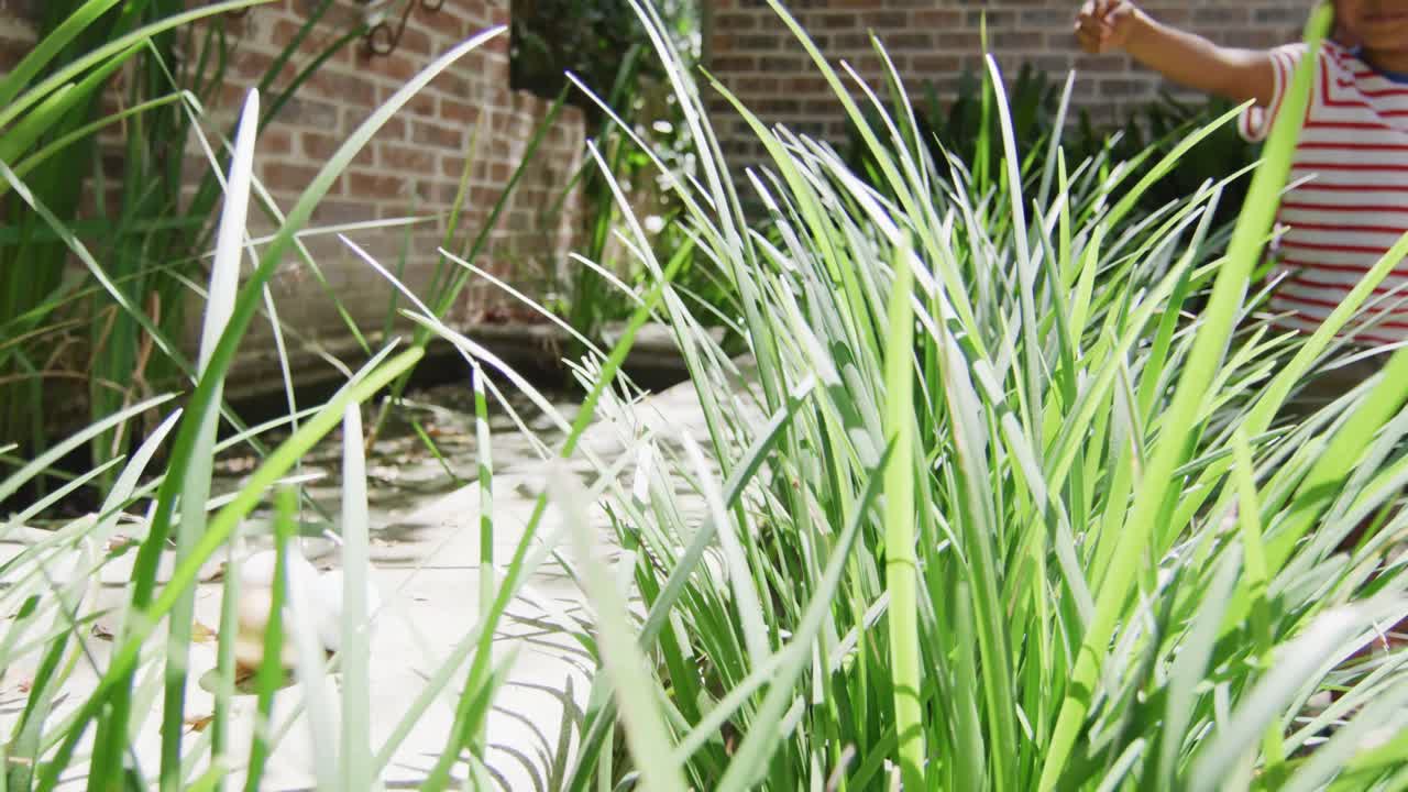 счастливый афроамериканский брат и сестра охотятся на пасхальные яйца в солнечном саду, в замедленном режиме