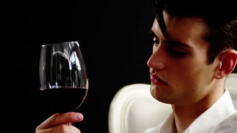 Androgynous-man-holding-wine-glass-against-black-background