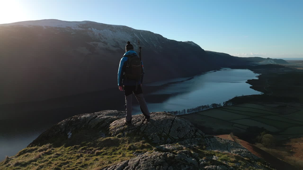 excursionista en afloramiento rocoso con revelación de lago oscuro y valle verde más montañas nevadas y destello de lente natural en el distrito de lagos wasdale reino unido