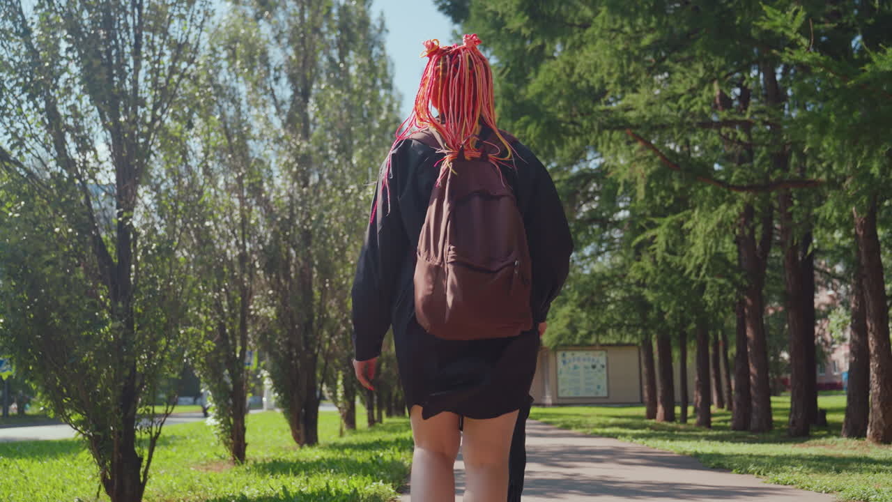 Una persona se mueve con determinación por un sendero arbolado; se aleja con tranquilidad en un parque sombreado por árboles; una mujer con un paraguas camina silenciosamente por el sendero de un parque iluminado por el sol y rodeado de follaje.