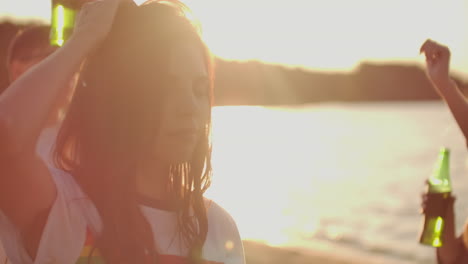 a happy young girl in a short white t-shirt with a rainbow is dancing on the beach party with her friends and beer. her hair is flying on the wind. she enjoys partytime with her eyes closed.