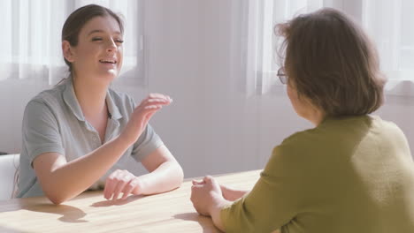 anciana y doctora sentadas en una mesa hablando entre ellas 1